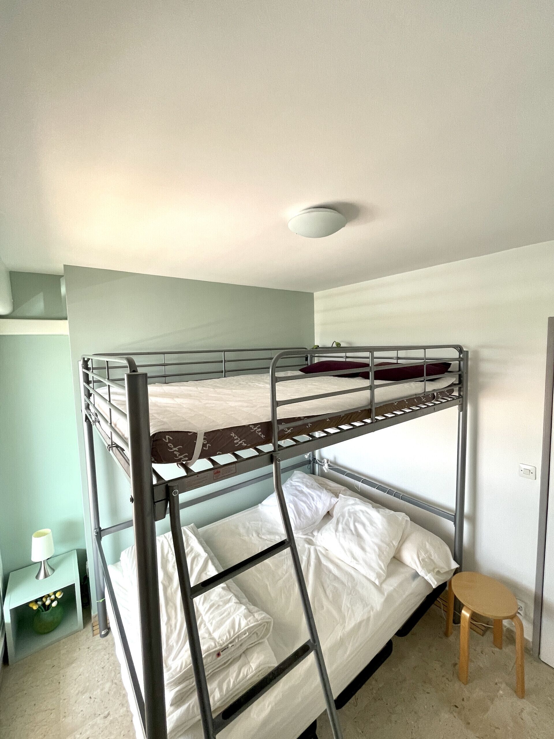 Une chambre avec un lit superposé, un lit simple en bas et un interrupteur sur le mur.