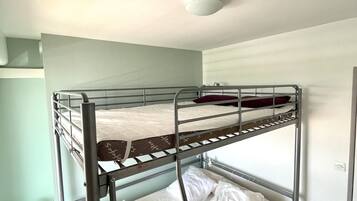 Une chambre avec un lit superposé, un lit simple en bas et un interrupteur sur le mur.