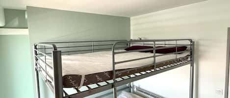 A bunk bed room with a single bed on the bottom bunk and a light switch on the wall.