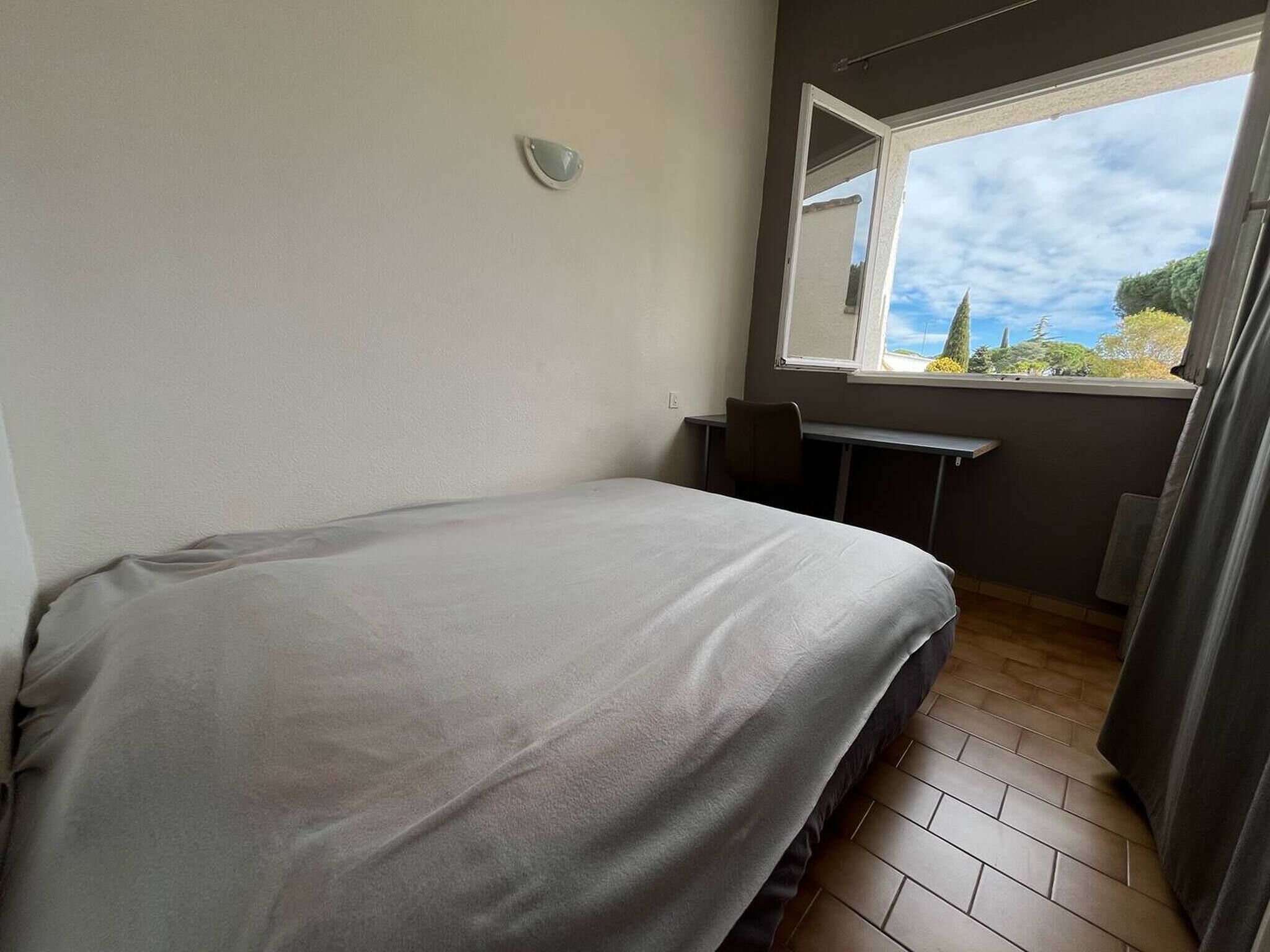 Un dormitorio con una cama, un escritorio y una ventana que da a vistas de árboles y cielo.