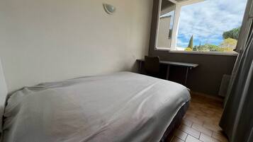 Un dormitorio con una cama, un escritorio y una ventana que da a vistas de árboles y cielo.