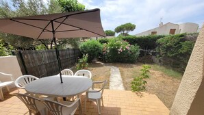 An outdoor patio with a round table and chairs, a large umbrella, and a brick pathway leading to a garden. - Quartier des Goélands, Villa t5 pour 8 N25 (La Grande-Motte)
