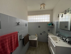 Une salle de bain avec une baignoire, un lavabo, un miroir et une fenêtre.