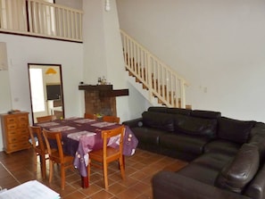 A living room with a dining table, chairs, a black leather sofa, and a staircase.