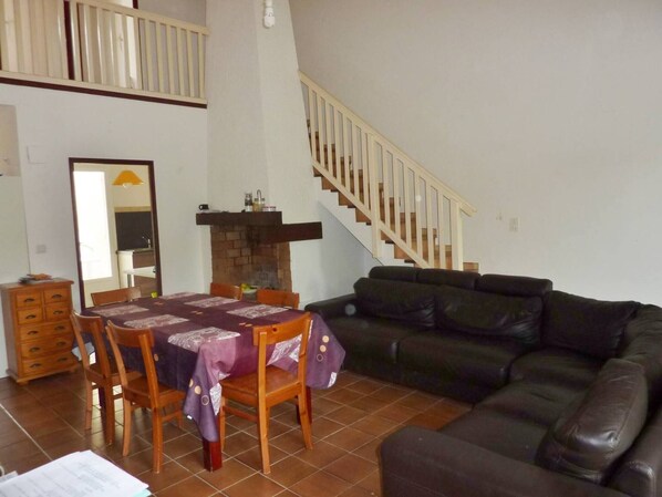 A living room with a dining table, chairs, a black leather sofa, and a staircase.