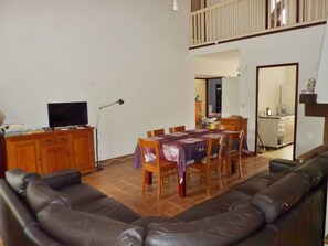 A living room with a sofa, a dining table with chairs, a TV, and a lamp.