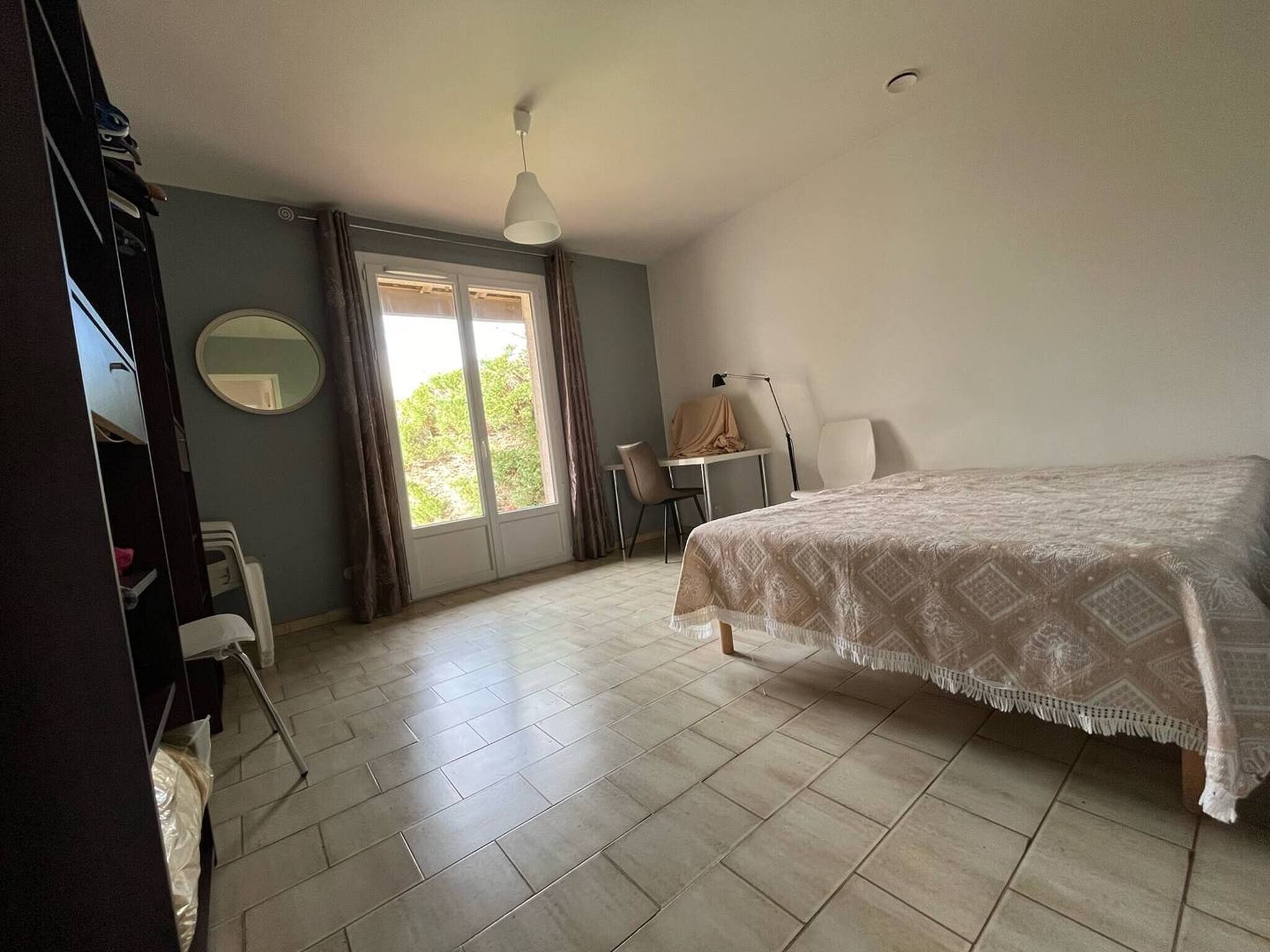 Un dormitorio con cama, escritorio, silla, lámpara, espejo y ventana.