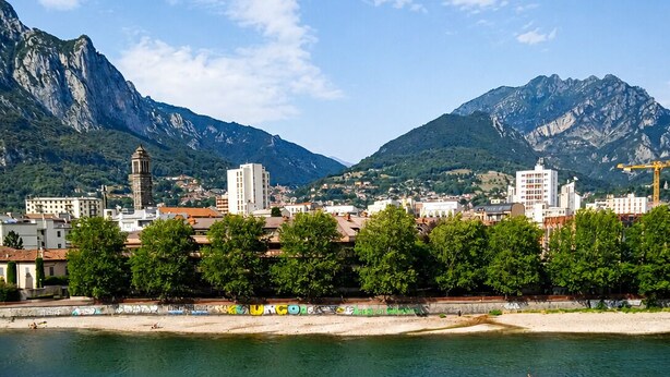 Une ville côtière traversée par une rivière, bordée de montagnes, et offrant une vue depuis un balcon doté d’une balustrade.