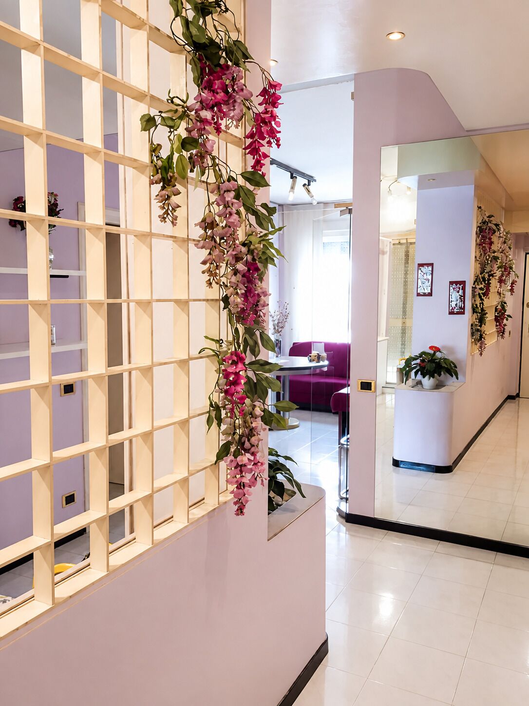 En modern inredning med en vit hyllsektion, en hängande blomsterdekoration och en sittgrupp med en lila soffa.