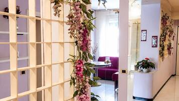 En modern inredning med en vit hyllsektion, en hängande blomsterdekoration och en sittgrupp med en lila soffa.