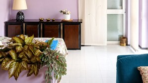 Une chambre avec un lit, une table de chevet avec une lampe, une petite plante et une fenêtre avec des rideaux.