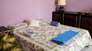 Une chambre à coucher avec une couvre-lit à motifs floraux, une table de chevet avec une lampe et une petite table de nuit avec une plante.