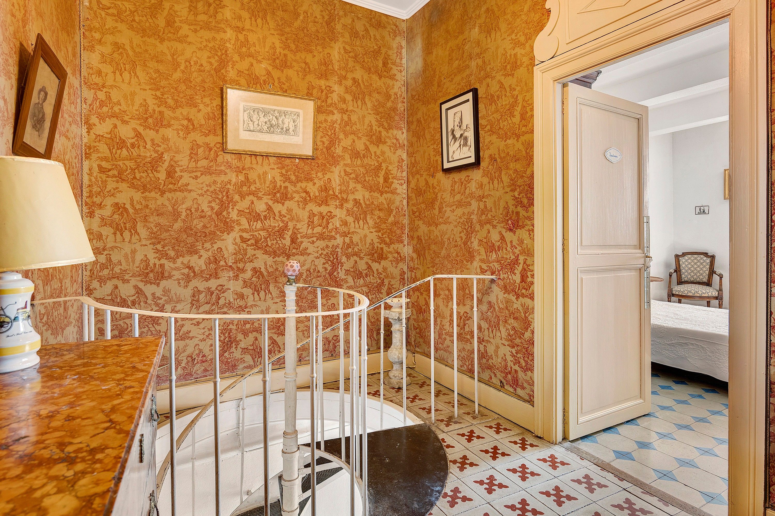 A room with a staircase, a door leading to another room, and a patterned wallpaper.