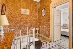 A room with a staircase, a door leading to another room, and a patterned wallpaper.