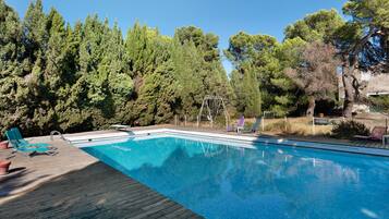 A swimming pool with a wooden deck, surrounded by trees and equipped with lounge chairs.