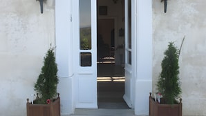 A building entrance with a white door, two potted plants, and wall-mounted lights.