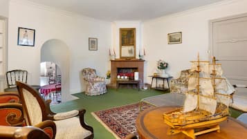 A room with a round wooden table, a ship model, and a fireplace with a mantel.