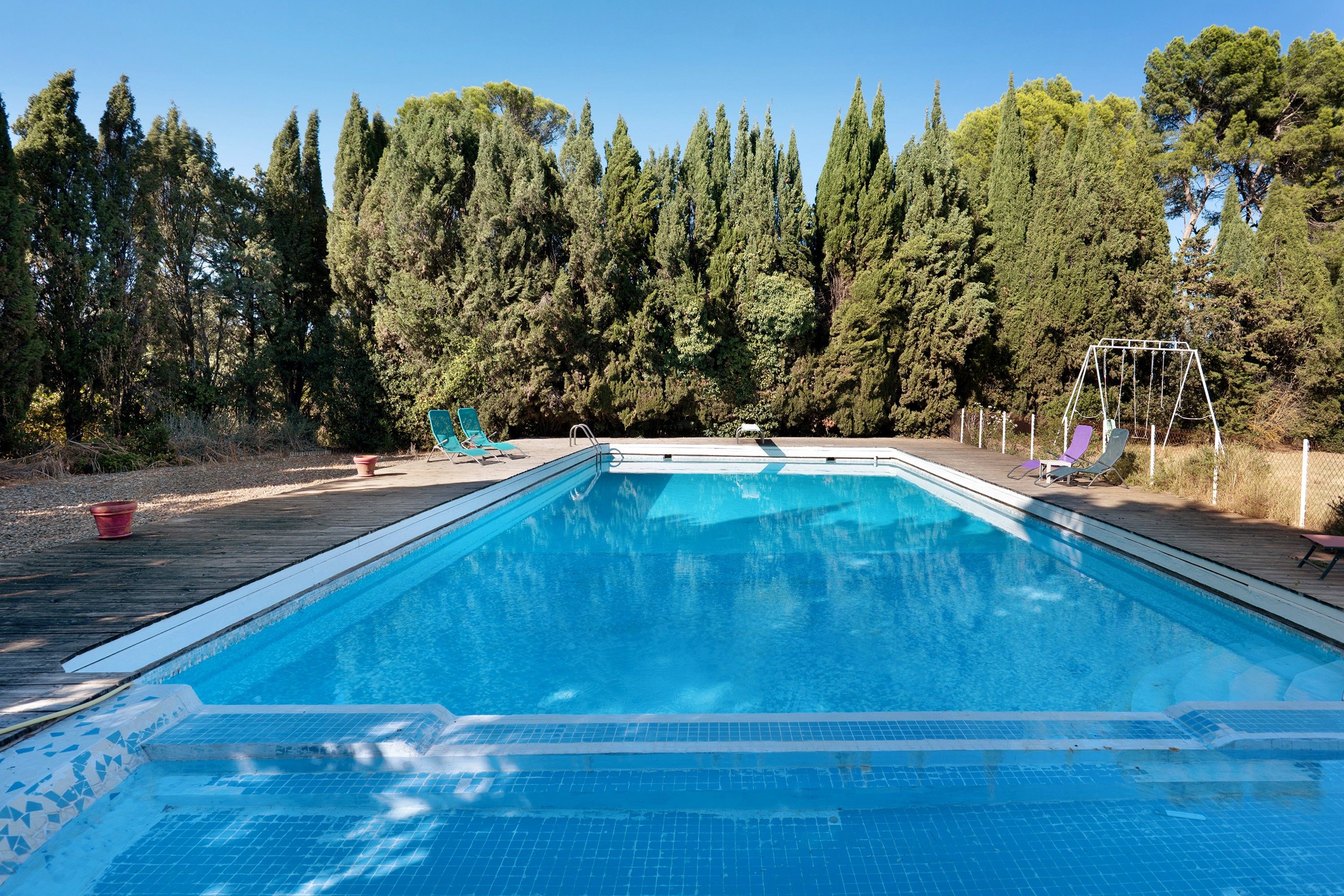 Une piscine rectangulaire dont les bords sont recouverts de carreaux, entourée d’une terrasse en bois.