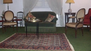 A room with a green sofa, two armchairs, a small table, a patterned rug, a window with sheer curtains, and two lamps.