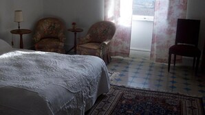 A hotel room with a bed, two armchairs, a small table, a TV, and a view of the outdoors. - Bed and Breakfast 'Chambre Isabeau' with Shared Pool, Shared Garden and Wi-Fi (Carcassonne)