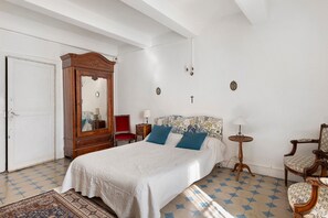 Un dormitorio con una cama grande, un armario de madera, una silla roja, una mesita pequeña y un cabecero estampado.