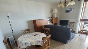 A compact living space with a dining table, chairs, a sofa, a TV, and a lamp. - Coeur de ville, t3 pour 6 personnes N35 (La Grande-Motte)