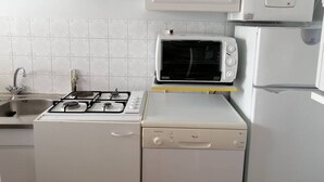 A compact kitchen with a gas stove, a microwave, a built-in oven, and a refrigerator. - Coeur de ville, t3 pour 6 personnes N35 (La Grande-Motte)