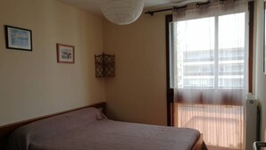 A bedroom with a bed, a window with curtains, and two framed pictures on the wall. - Coeur de ville, t3 pour 6 personnes N35 (La Grande-Motte)