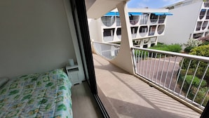 A balcony with a bed, a white railing, and a view of neighboring buildings.