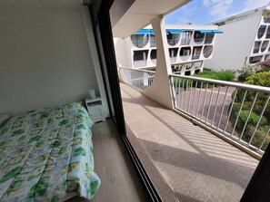 A balcony with a bed, a white railing, and a view of neighboring buildings.