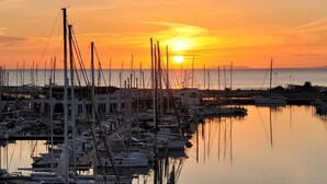 A marina with multiple boats docked, a clear sky, and the sun setting in the background.