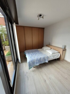 A bedroom with a bed, wooden wardrobe, and a window.