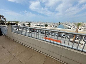 A balcony with a view of a marina filled with boats, a clear sky, and a few palm trees.