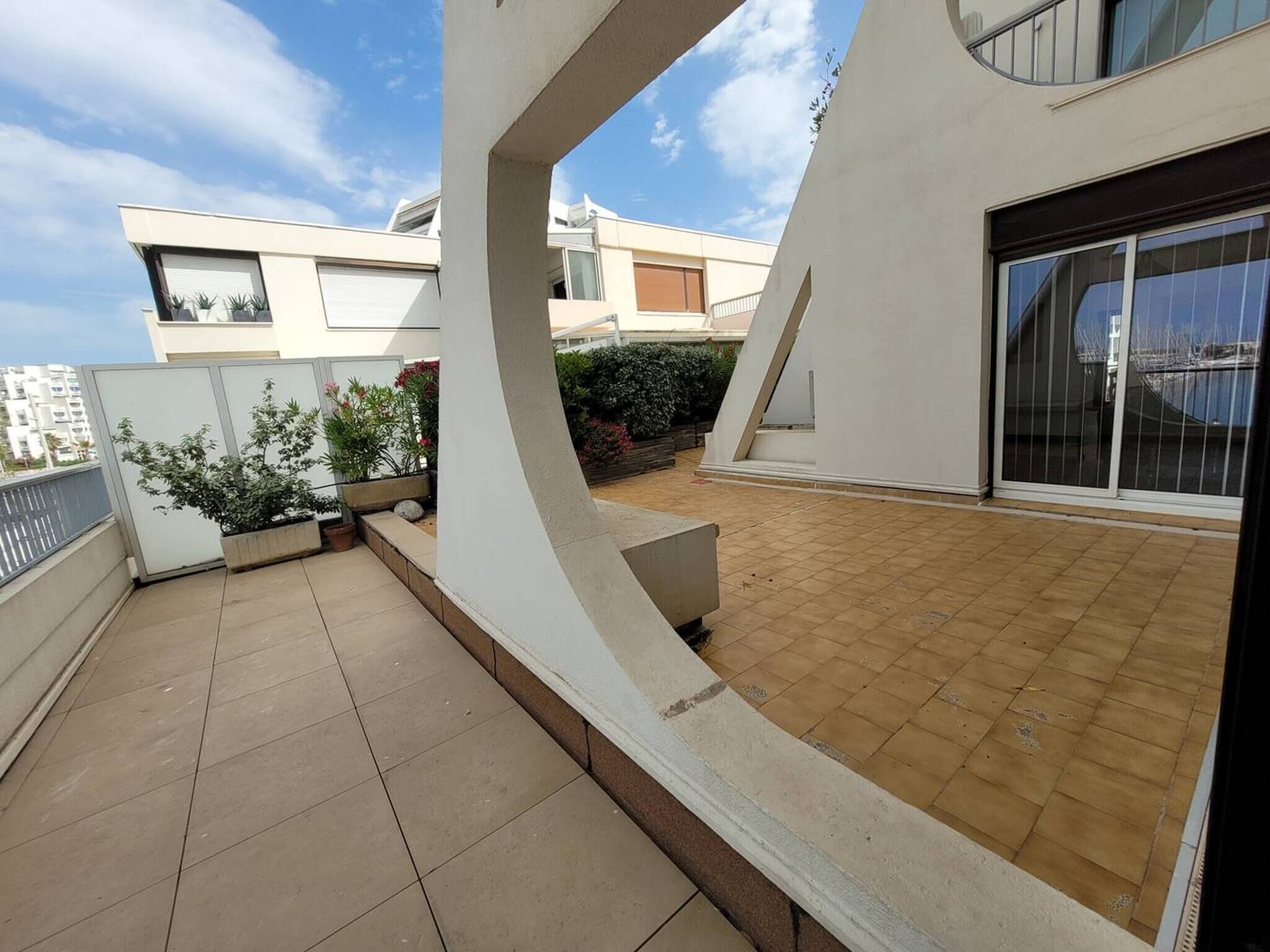 Un immeuble résidentiel moderne doté d’un patio carrelé, d’un petit jardin et d’un balcon offrant une vue sur le quartier environnant.