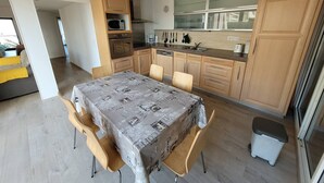 A modern kitchen with wooden cabinets, a dining table with chairs, and a view of the outside. - Quartier du port, t4 pour 8 personnes N12 (La Grande-Motte)
