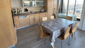 A modern kitchen with a dining area, wooden cabinets, and a view through large windows.