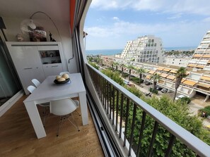 Ein Balkon mit Esstisch, Stühlen und einer dekorativen Schale. Durch die Brüstung ist die Stadt und das Meer zu sehen.