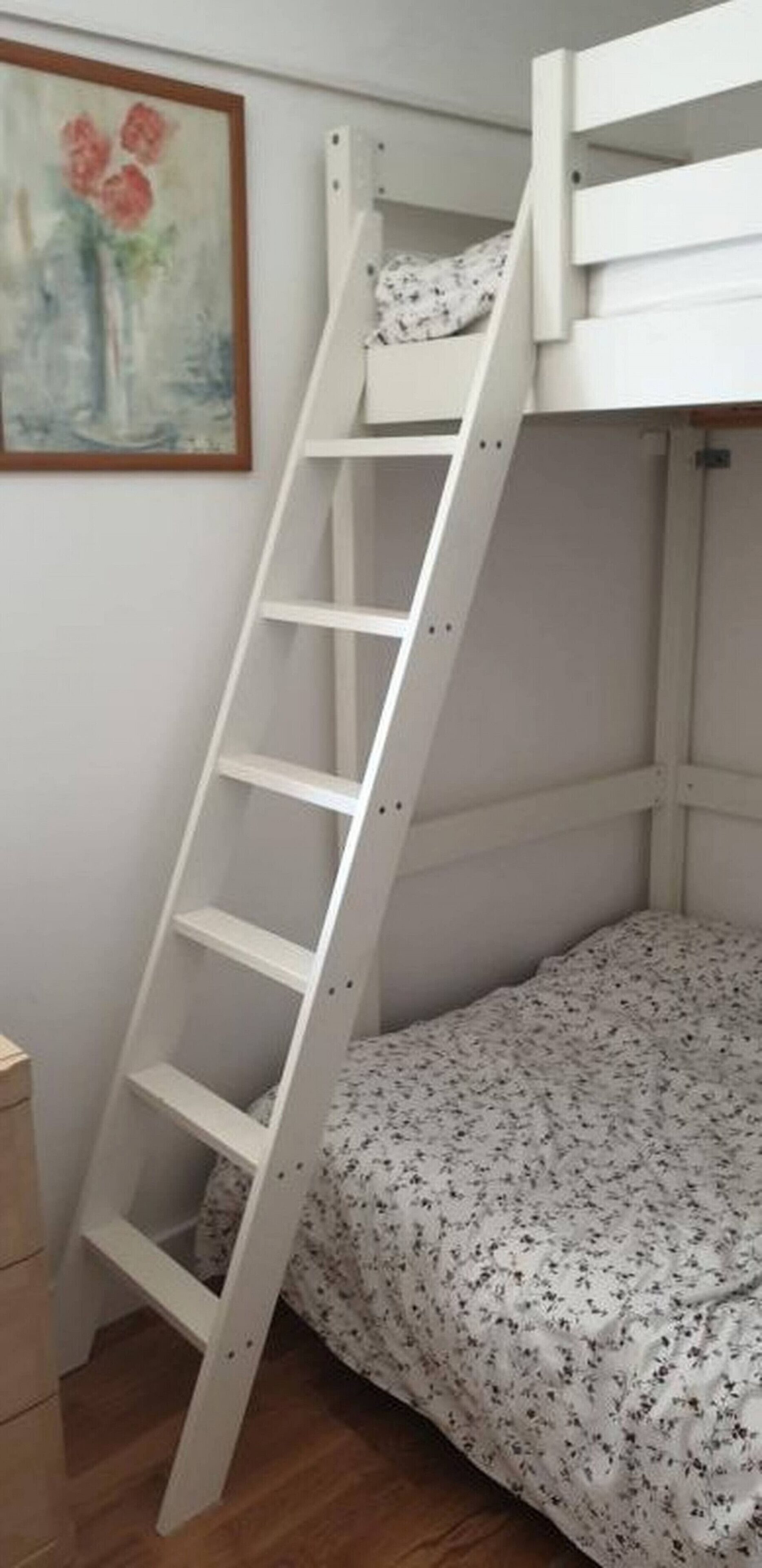 Un lit superposé avec une échelle blanche, une couvre-lit à motifs floraux et un tableau accroché au mur.