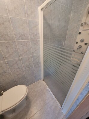 A bathroom with a toilet, a shower with a glass door, and tiled walls. - Au centre de la Grande Motte, t3 pour 5 N24 (La Grande-Motte)
