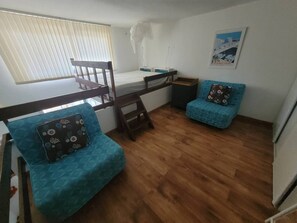 Ein kleines Zimmer mit Etagenbett, Tisch, Stuhl und Schlafsofa.