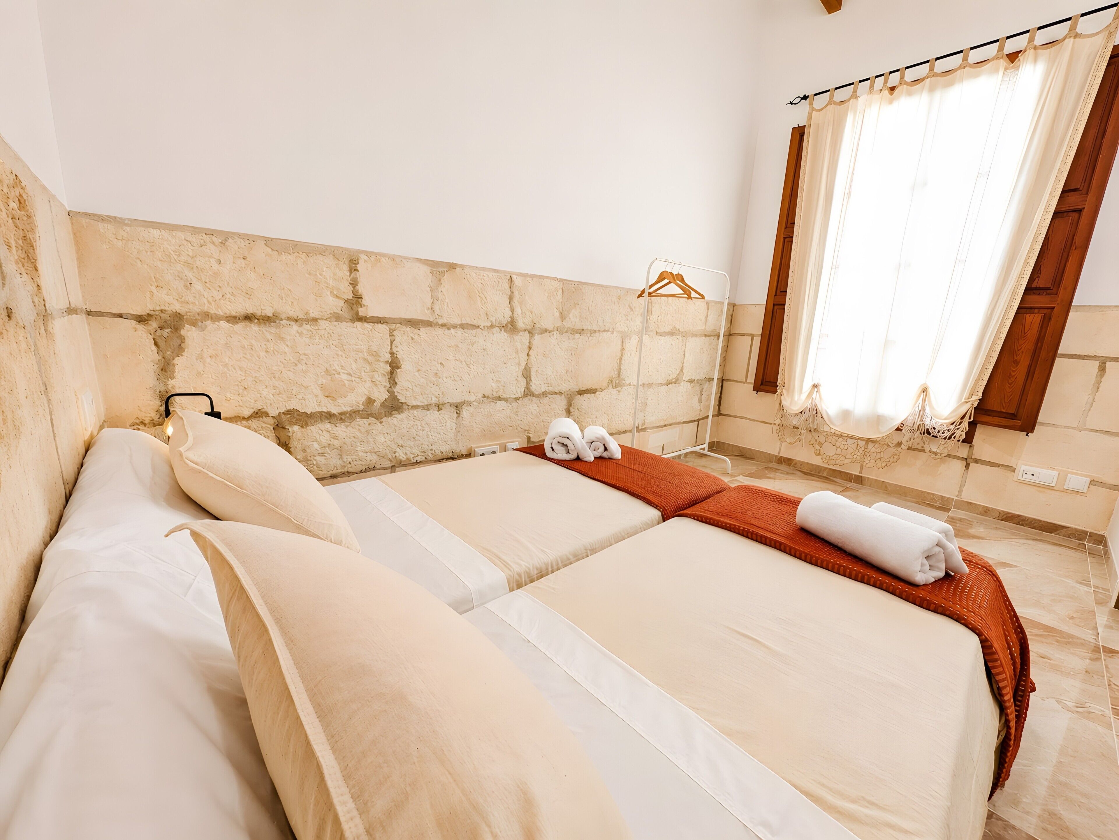 A hotel room with two beds, a stone headboard, a window with curtains, and a wooden door.