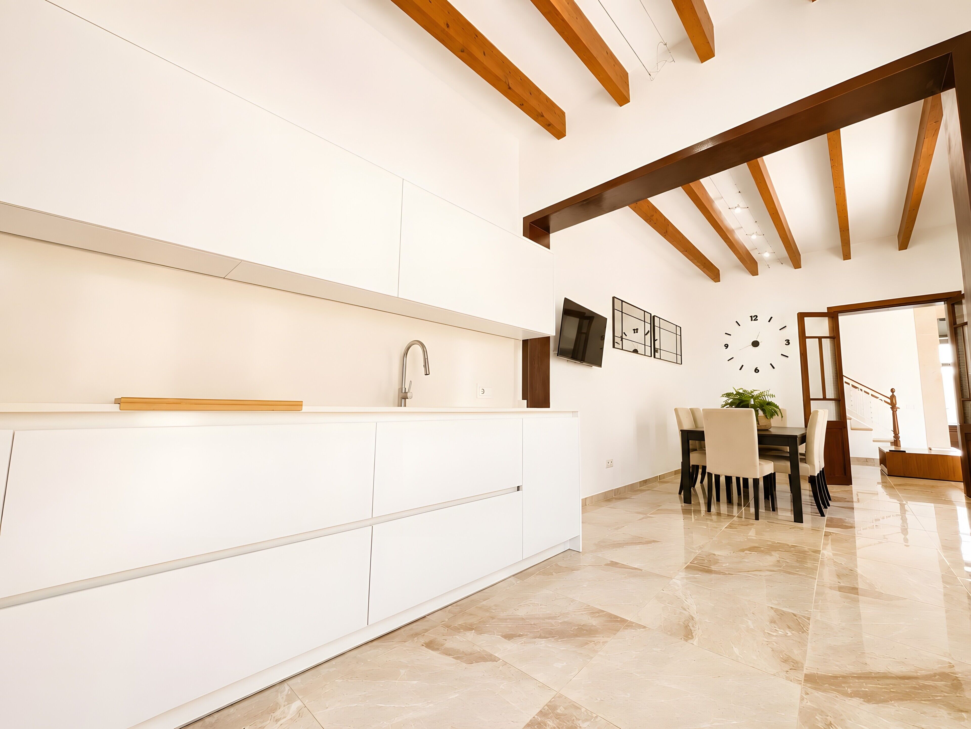 A modern kitchen with white cabinetry, a built-in sink, and a dining area with a table and chairs.