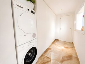 Una sala de bugaderia amb una rentadora i assecadora de càrrega frontal, un paviment de rajoles i una porta que dona a una altra habitació.