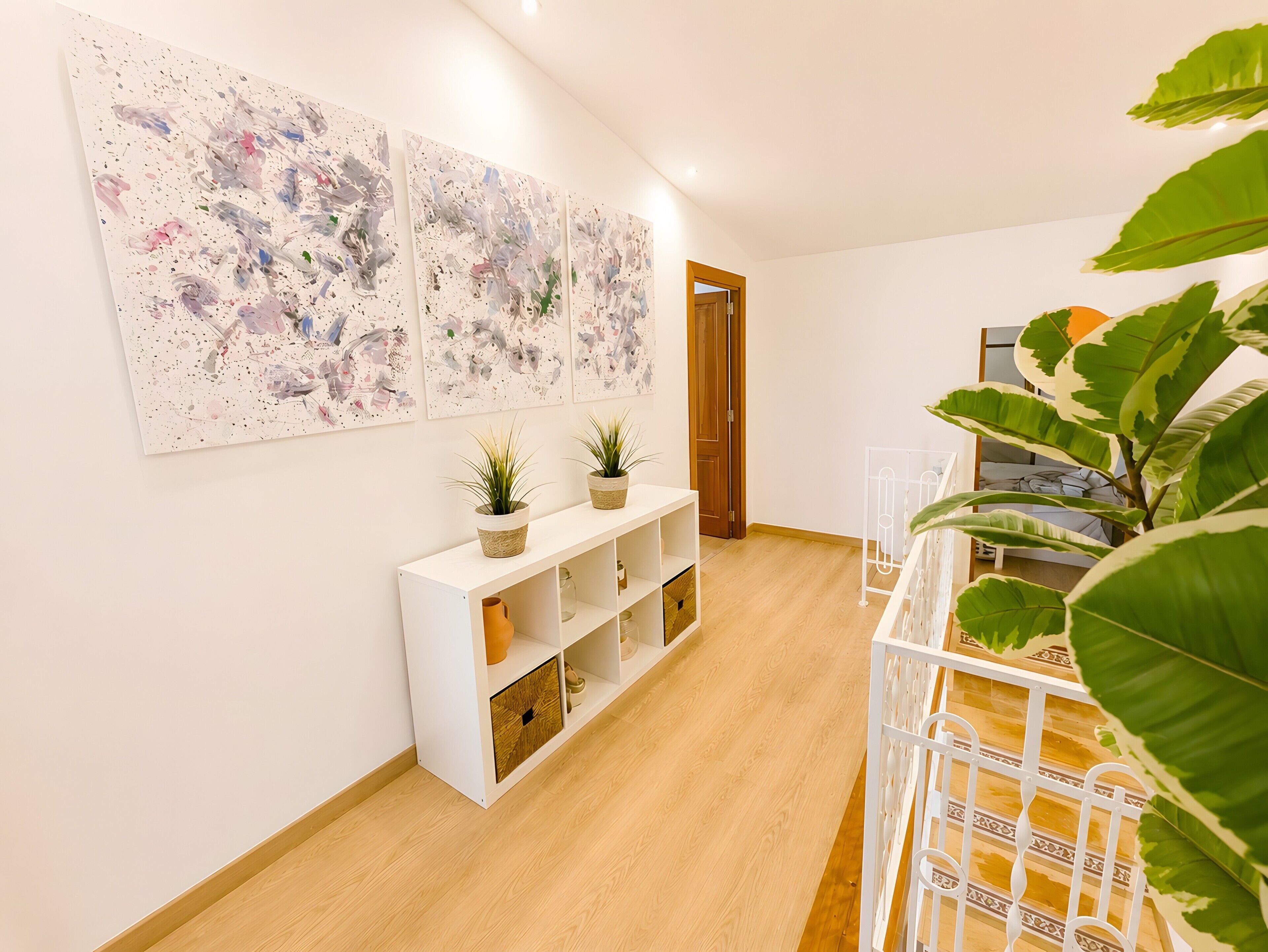 A hallway with a white console table, potted plants, and abstract wall art.