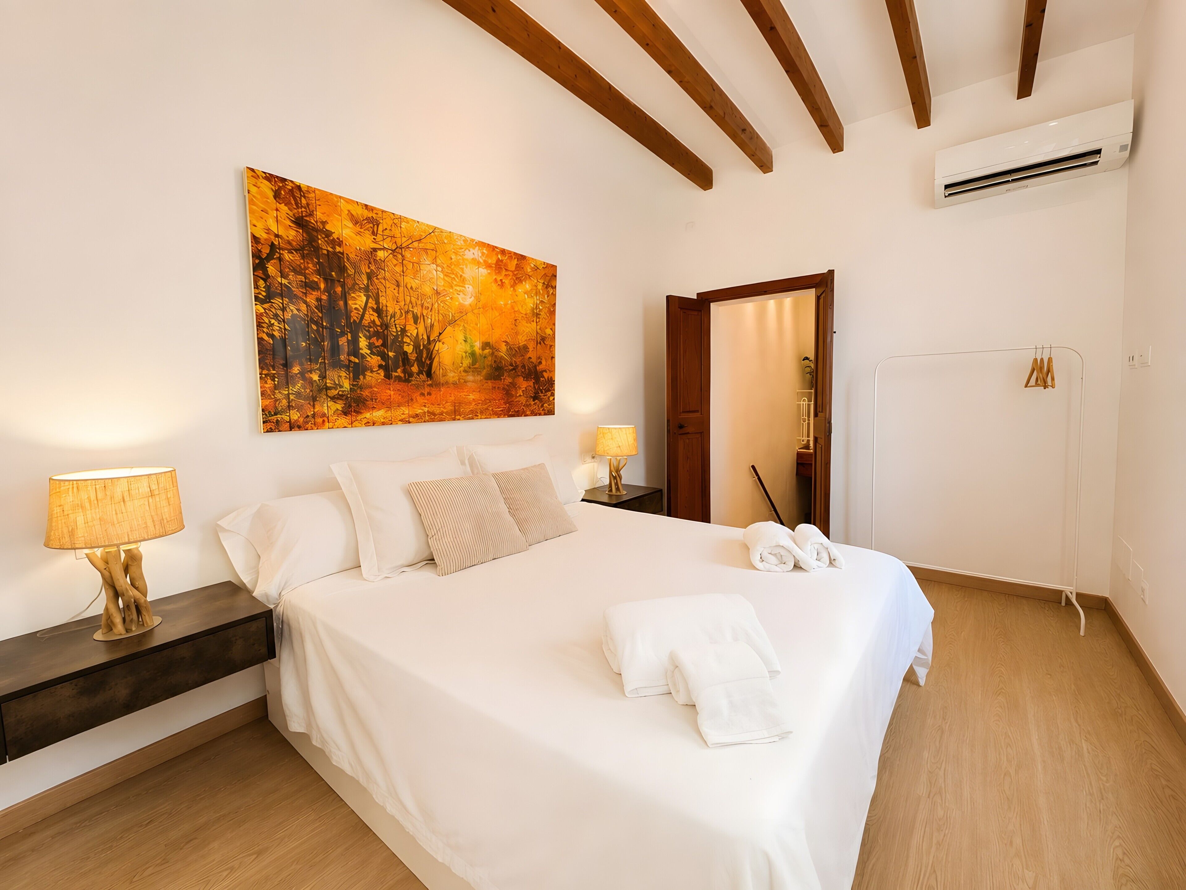 A neatly made bed with white linens, a wooden headboard, and a painting above it.