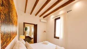 A hotel room with a bed, a painting, a window with curtains, and a wooden ceiling. - Ca na Victòria: Mallorcan Home with Wi-Fi and Air Conditioning (Santa Margalida)