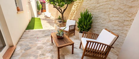 Un patio exterior con suelo de piedra, muebles de madera y plantas en macetas.