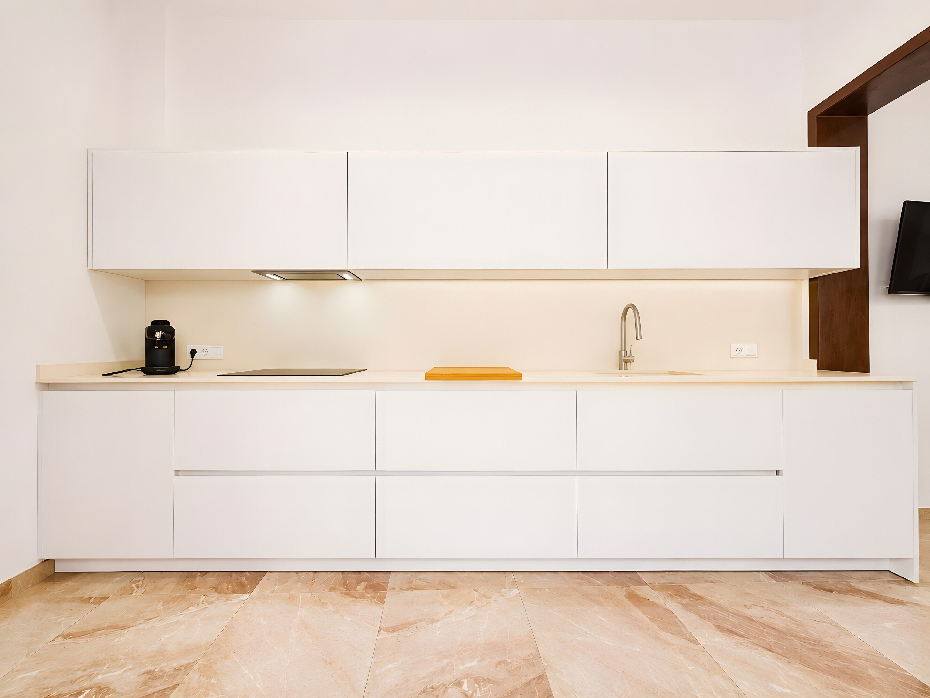 Una cocina moderna con armarios blancos, una cafetera negra y una tabla de cortar de madera.