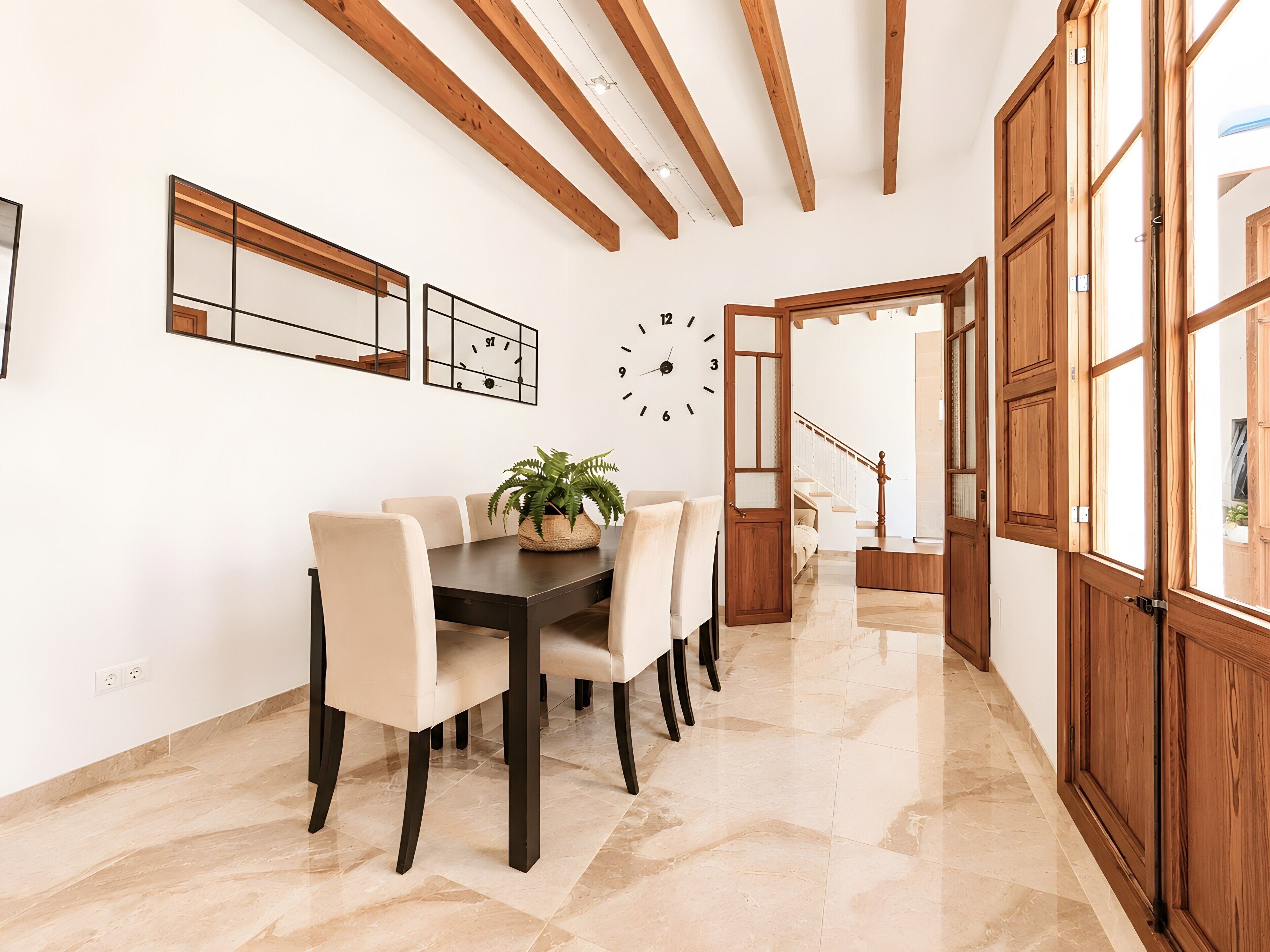 A dining area with a table and chairs, a clock, and wooden beams on the ceiling.