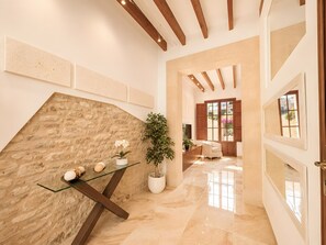 A spacious hallway with a stone wall, a glass table with decorative items, a potted plant, and a view of a room with a window. - Ca na Victòria: Mallorcan Home with Wi-Fi and Air Conditioning (Santa Margalida)